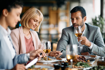 Smiling businesswoman eating while having lunch with colleagues in restaurant.