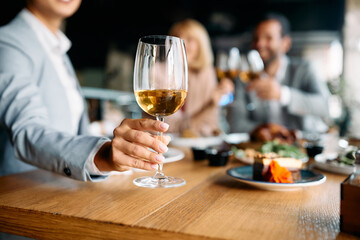 Close up of businesswoman taking glass of wine while toasting with her colleagues in restaurant.