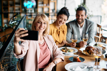 Happy businesswoman taking selfie with her colleagues while having lunch in restaurant.