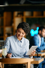 Happy businesswoman working on touchpad and taking notes in cafe.