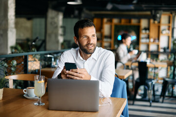 Obraz premium Pensive businessman using cell phone and listening music over earphones in cafe.
