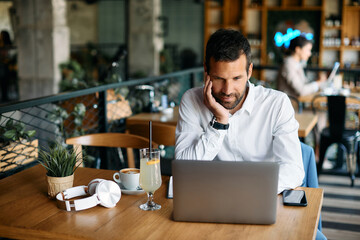 Obraz premium Smiling businessman reading e-mail on laptop in cafe.