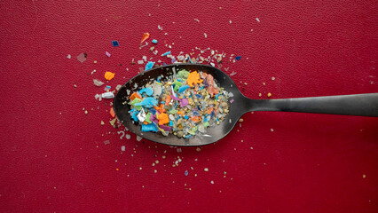 A pile of microplastics gathered from the beach in a spoon against a dark red background. Concept...