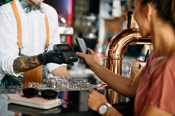 Fototapeta na wymiar Close up of woman using mobile phone while paying at bar counter.