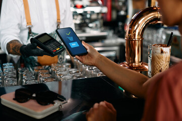 Close up of woman paying with smart phone at bar counter.