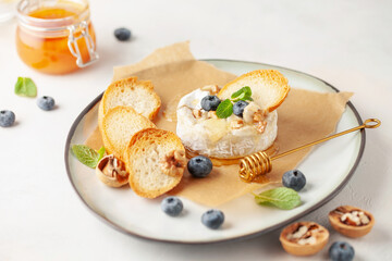 Traditional baked brie cheese or camembert with honey, nuts, blueberries and mint leaves, with breadcrumbs.