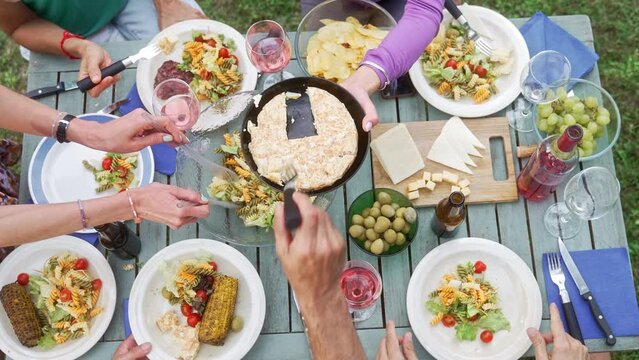 Top View Of People Hands Sharing healthy food, vegetarian organic pasta salad, delicious wine around rustic garden table in summer having dinner party 