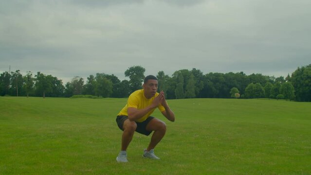 Athletic handsome African man doing squats to broad jump exercise, strengthening lower body muscles, improving stability and balance, increasing heart rate while working out in nature.