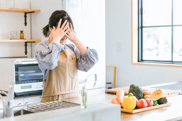 キッチンにいる料理が苦手なエプロン姿の女性（悩む・困る）
