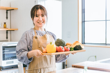野菜を持ってキッチン立つエプロン姿の日本人女性
