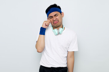 young Asian sportman in blue headband and white t-shirt with headphones, rubs tears wants to cry feels depressed has a problem isolated on white background. Workout sport concept