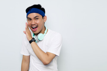 Excited young Asian sportman in blue headband and sportswear white t-shirt with headphones, whispering gossip and  sharing news isolated on white background. Workout sport concept