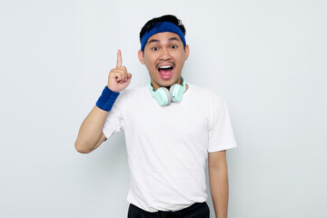 Excited young Asian sportman in blue headband and sportswear white t-shirt with headphones, pointing fingers up having a good idea isolated on white background. Workout sport concept
