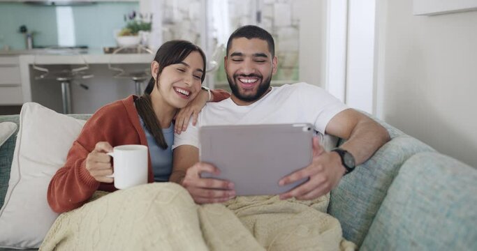 A young latin couple using a digital tablet and laughing while watching a comedy movie. A young man and woman watching videos and bonding together indoors. People browsing social media online