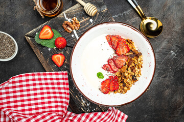 Granola with yogurt with fresh strawberry, chia seeds and honey on a dark background. Delicious balanced food concept