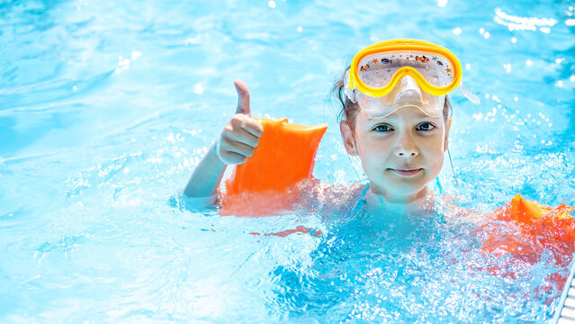 Close-up portrait of a cute little Caucasian girl swimming in the pool in a swimming mask and armbands, beach resort, summer vacation concept. Space for text.