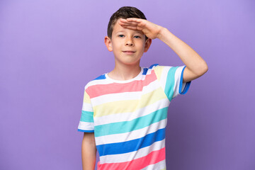 Little boy isolated on purple background saluting with hand with happy expression