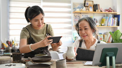 Female potter taking photo of ceramics product for upload to website online shop. Online selling, E-commerce concept