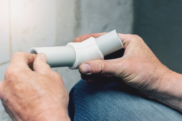 A plumber holds polypropylene pipes connected at right angles in his hands