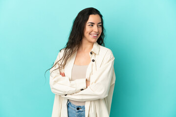 Young caucasian woman isolated on blue background with arms crossed and happy