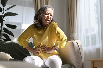 Unhealthy middle aged lady touching belly, suffering from abdomen ache, symptoms gastrointestinal...