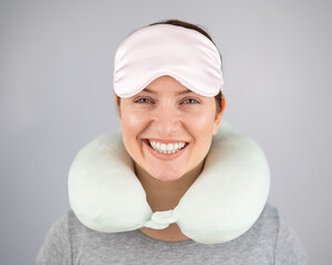 Smiling caucasian woman with travel pillow and sleeping mask isolated on white background.