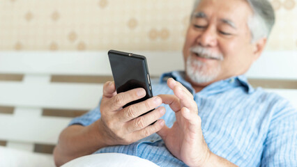 Senior Male using a smartphone , smiling feel happy in bed at home - lifestyle senior concept - select focus and blur photography