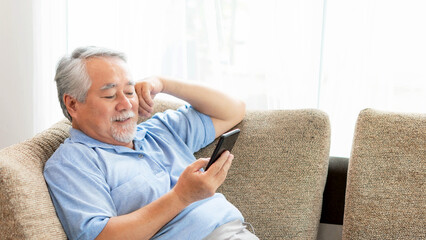 Fototapeta premium Senior Male using a smartphone , smiling feel happy on sofa at home - lifestyle senior concept
