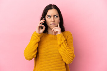 Young caucasian woman using mobile phone isolated on pink background having doubts and thinking