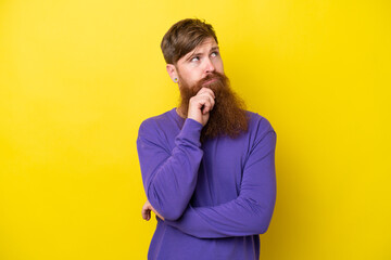 Redhead man with beard isolated on yellow background thinking an idea while looking up