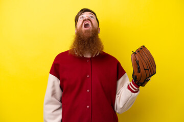 Redhead player man with beard with baseball glove isolated on yellow background looking up and with...