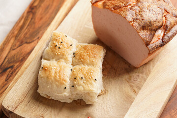 Traditional oven baked bavarian meal leberkäse sliced - meat dish made of corned beef, pork and bacon, finely ground and bakes as a bread loaf, on wooden board on dark wooden table with bread cubes