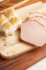 Traditional oven baked bavarian meal leberkäse sliced - meat dish made of corned beef, pork and bacon, finely ground and bakes as a bread loaf, on wooden board on dark wooden table with bread cubes