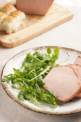 Traditional oven baked bavarian meal leberkäse sliced - meat dish made of corned beef, pork and bacon, finely ground and bakes as a bread loaf, served on a plate with greed arugula leaves