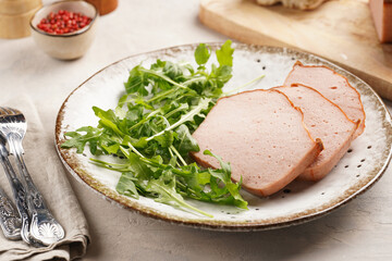 Traditional oven baked bavarian meal leberkäse sliced - meat dish made of corned beef, pork and bacon, finely ground and bakes as a bread loaf, served on a plate with greed arugula leaves