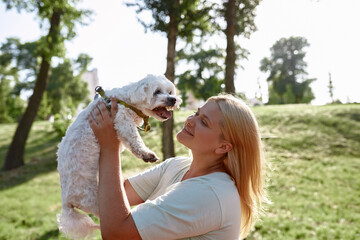 Girl hold and look at Maltese dog in blurred park
