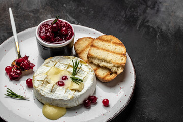 French cuisine. Baked camembert cheese with cranberries and basil leaves on a dark background, Long...