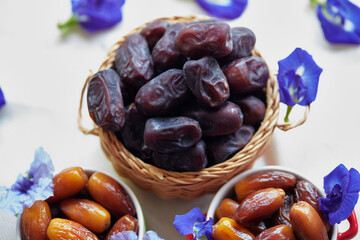 Dried dates in ceramic cup and wicker basket with fresh butterfly pea decoration