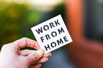 Naklejka na ściany i meble work from home sign being hold in front of out of focus lush green backard and home exterior, digital nomads working remotely or wfh days during lockdowns