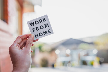work from home sign being hold in front of out of focus backyard and home exterior, digital nomads working remotely or wfh days during lockdowns