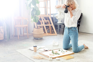 Woman photographer with a professional camera shoots perfume in a composition of plants, flowers...