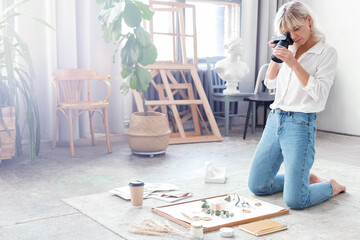 Fashionable girl with a professional camera shoots product in a composition of plants, flowers and fruit in her creative studio, for a portfolio or blog