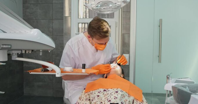 dentist work, male stomatologist in mask and gloves examines oral cavity of patient in dental office with professional equipment