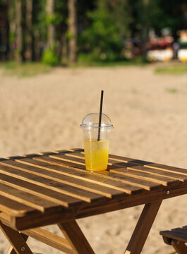 refreshing citrus drink in a plastic glass with a straw on a wooden table