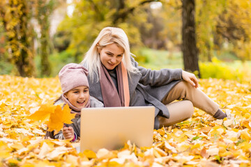 Beautiful young family lying on a picnic blanket, enjoying an autumn day in park while using laptop
