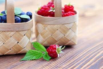 Fototapeta na wymiar blueberries and raspberries in small baskets made of birch bark on a wooden background. harvest of wild berries, vitamins and health benefits.