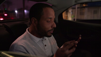 Passenger in the backseat of a car looking at cellphone device at night. One person staring at phone riding taxi