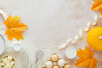 Autumn fall baking food background with pumpkins flour, milk, eggs, apples, butter, whisk for beating eggs on the apron. Cooking pumpkin or apple pie and cookies for Thanksgiving and autumn holidays