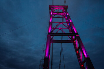 Illuminated pedestrian metal bridge on dark starry sky background, bottom view.
