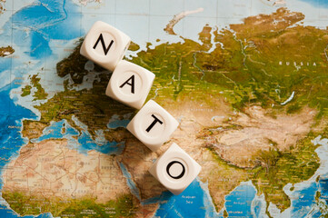 NATO spelled with dice on a world map, concept for the North Atlantic Treaty Organization expanding its members - obrazy, fototapety, plakaty